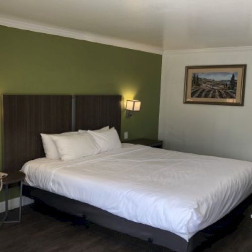 A hotel room with a large bed against a green accent wall, two wall lamps, side tables, a framed picture, and a view toward a bathroom area.