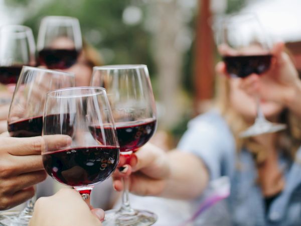 A group of friends toasting with red wine glasses, clinking together in a cheerful outdoor gathering.